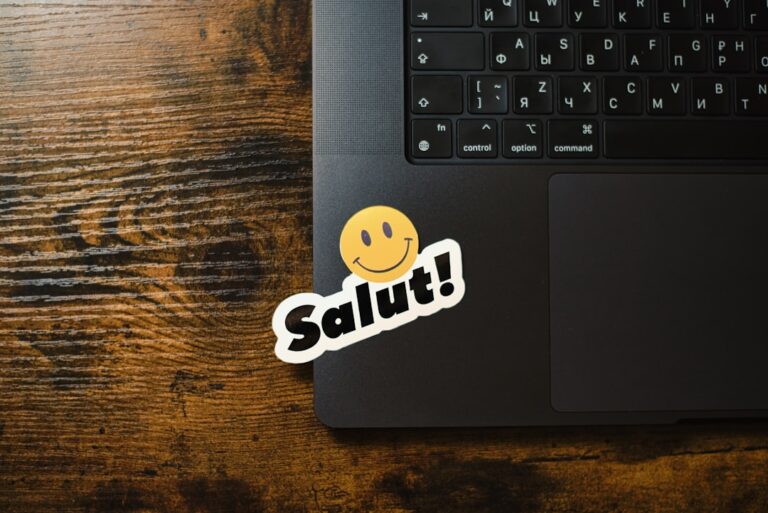 Laptop with a "salut!" smiley sticker on keyboard.