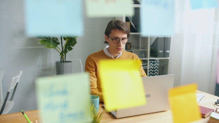 Man working on laptop surrounded by colorful sticky notes.