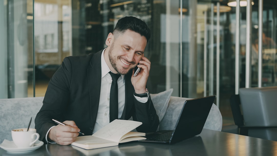 Man in suit talking on phone while writing.
