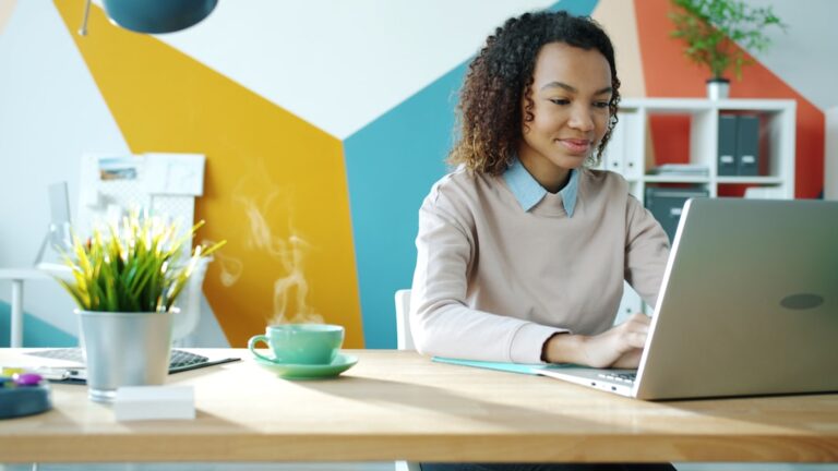 Young woman typing on laptop with coffee nearby